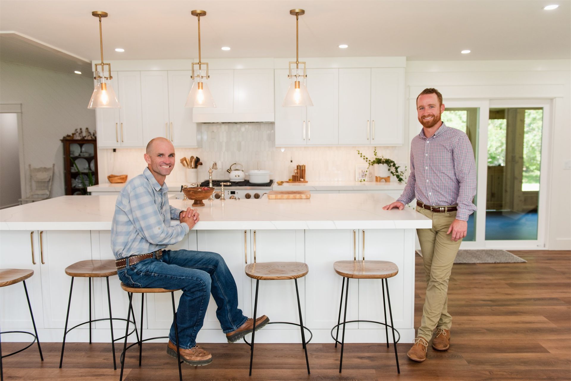 Two KMK Builders craftsmen in a finished custom white kitchen with brass pendant lighting.