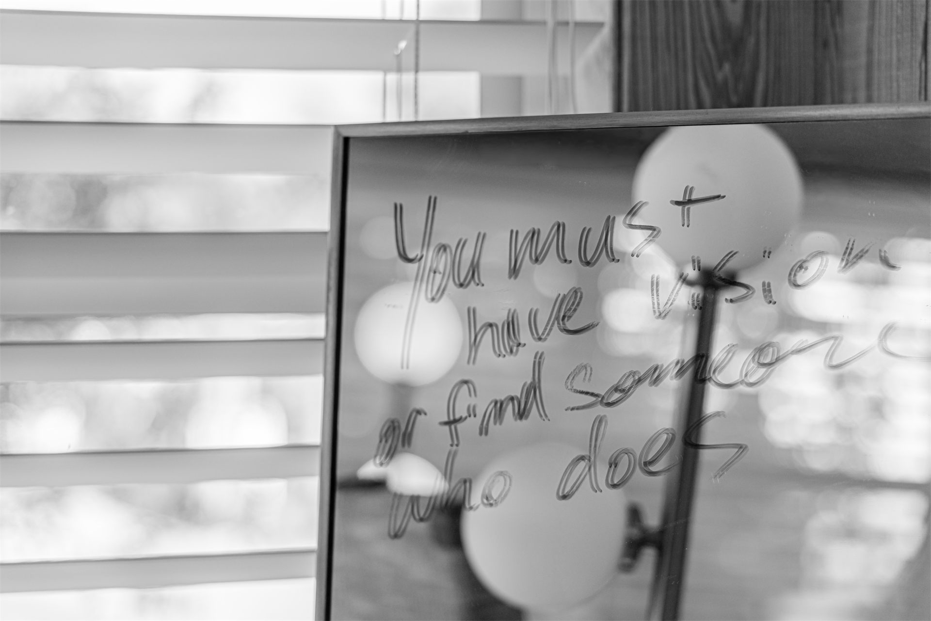 Black-and-white detail of a mirror inscribed 'You must have vision or find someone who does.'