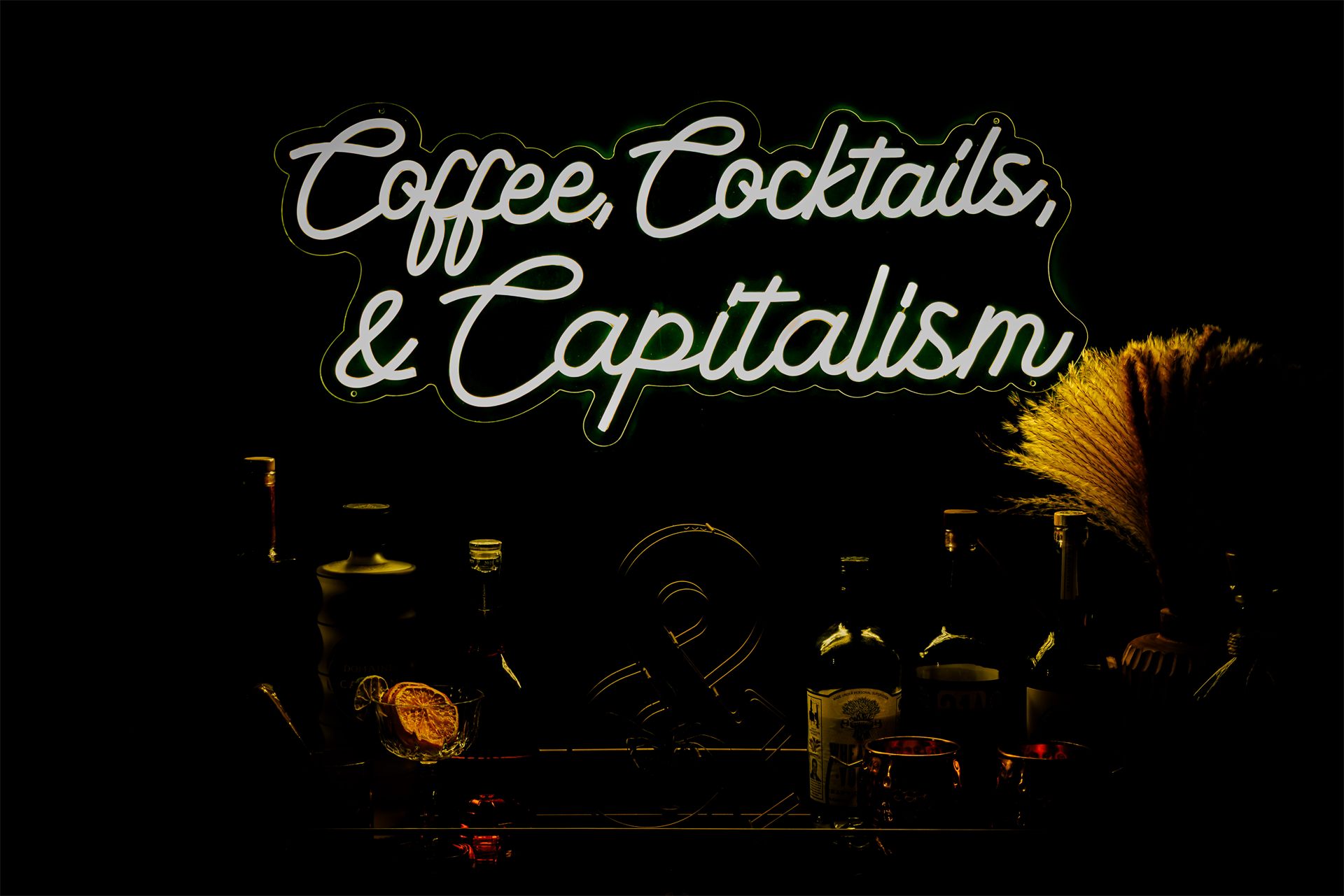 Styled studio bar cart beneath the glowing 'Coffee, Cocktails & Capitalism' neon sign.