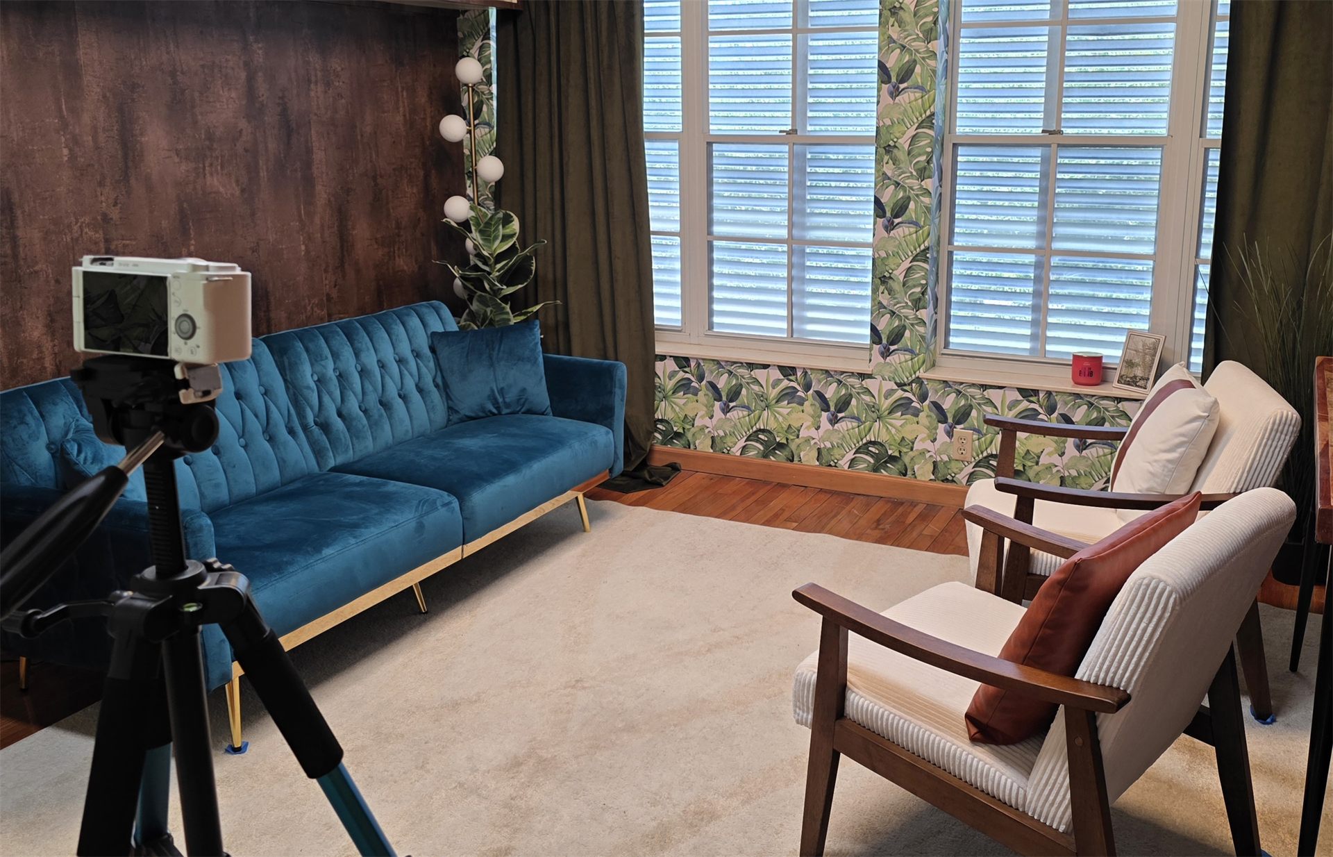 The Executive Content Studio—a warmly styled set with a teal velvet sofa, mid-century chairs, tropical accents, and a camera on a tripod.